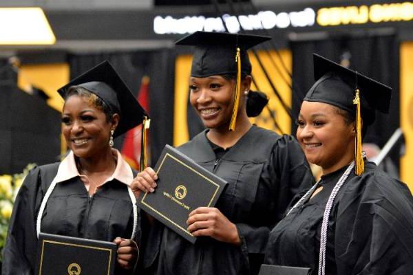 三名MCC女毕业生戴着帽子，穿着礼服，拿着毕业证书在毕业典礼上摆姿势.